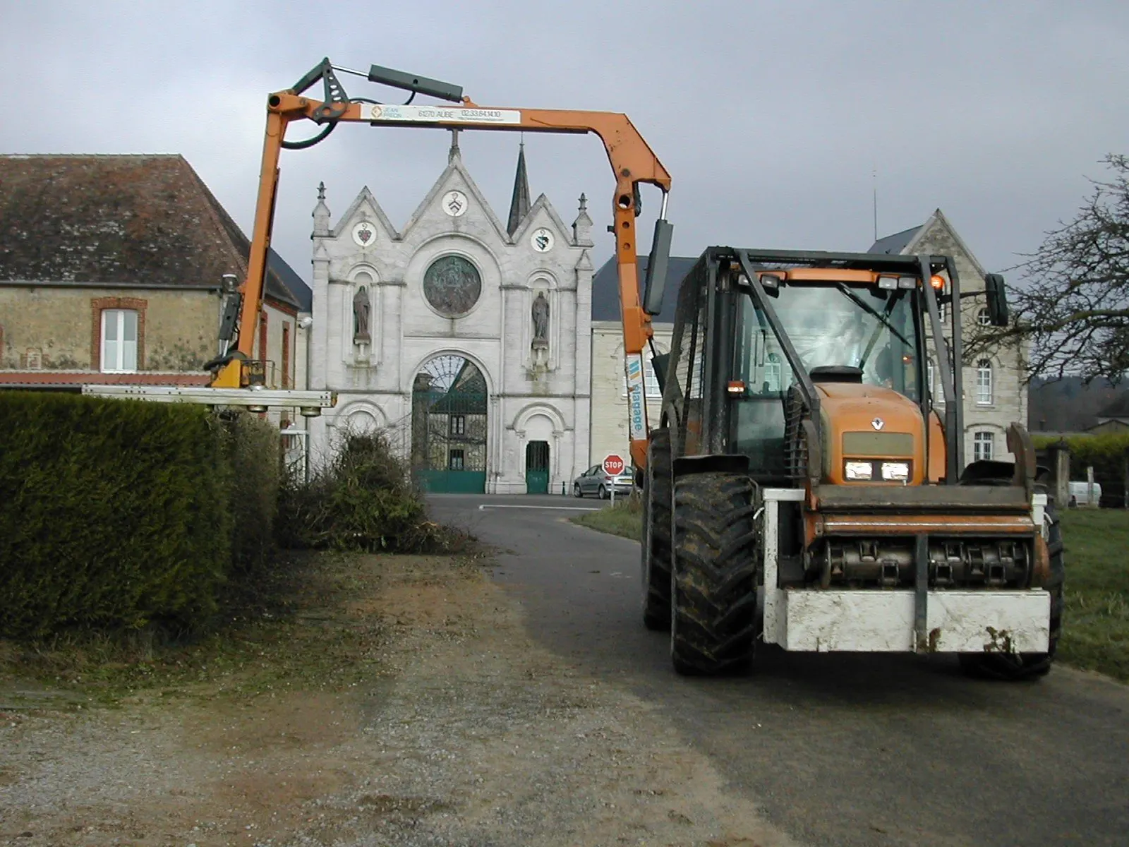 Lamier sur tracteur élaguant des arbres devant une abbaye