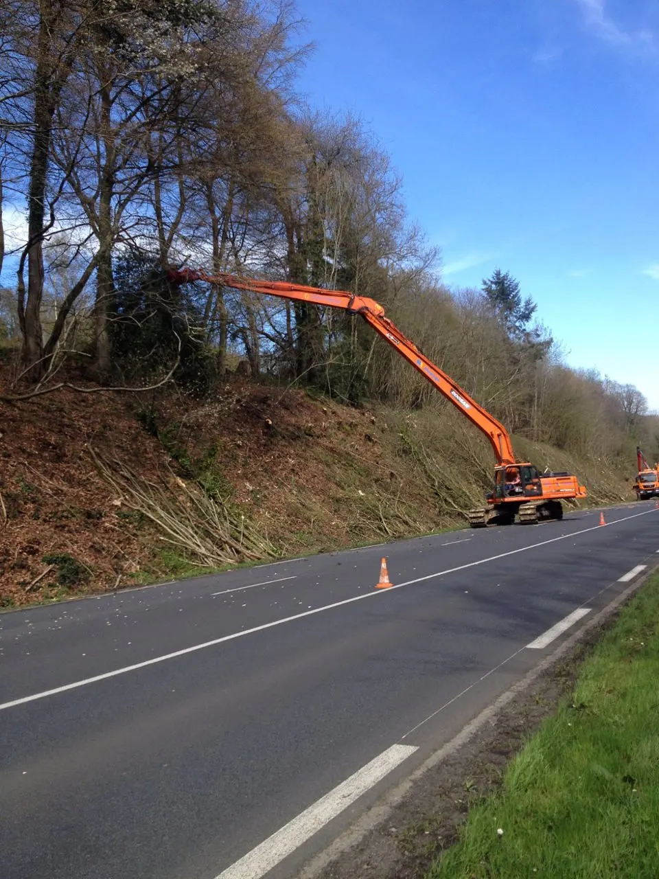 Pelle à long bras élaguant un talus boisé en bord de route